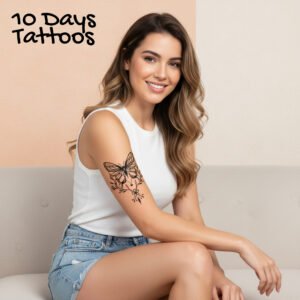 Tatouage temporaire papillon floral noir sur haut du bras d’une femme assise en débardeur blanc et short en jean 10 Days Tattoos