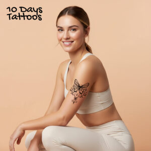 Tatouage temporaire papillon floral noir sur haut du bras d’une femme assise en tenue de sport beige 10 Days Tattoos