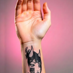 Gros plan main et avant-bras levés, tatouage temporaire Aku sur l'avant-bras, visage oni féminin kanji 悪 style gravure japonaise 14 × 6 cm, encre noire mat, fond rose corail